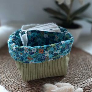 Petite panière en tissu vert contenant des lingettes textiles assorties.