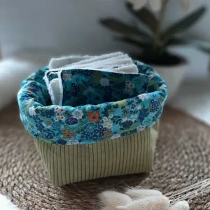 Petite panière en tissu vert contenant des lingettes textiles assorties.