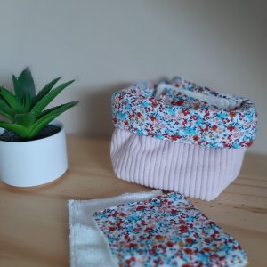 Petite panière en tissu rose contenant des lingettes textiles assorties.