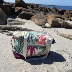 Sac week-end Sierra en version compacte, forme rectangulaire, avec mousquetons latéraux fermés. Motif tropical, base violette, posé sur le sable breton.