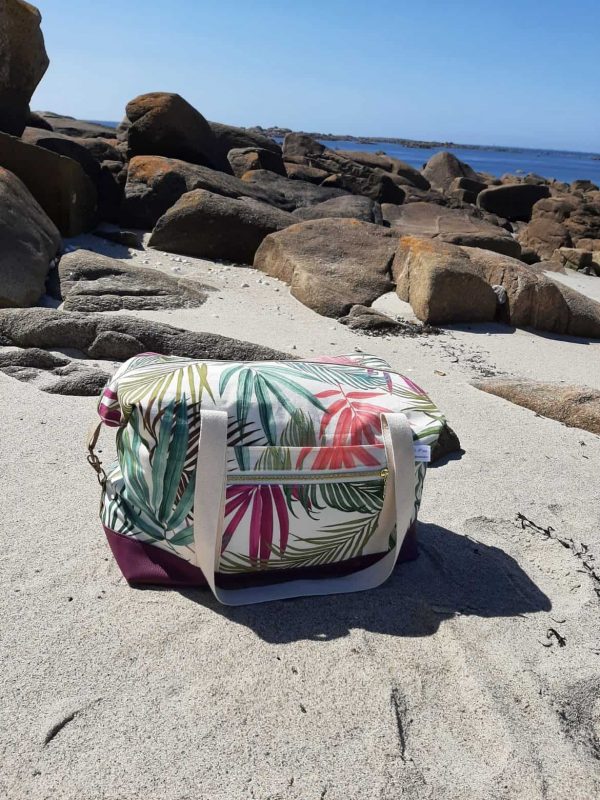 Sac week-end Sierra en version compacte, forme rectangulaire, avec mousquetons latéraux fermés. Motif tropical, base violette, posé sur le sable breton.