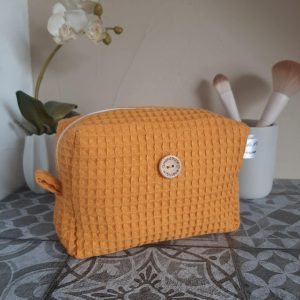 Trousse Essentiel en nid d'abeille moutarde, format compact avec zip doré et anse latérale. Un accessoire sobre et pratique pour ranger ses indispensables.