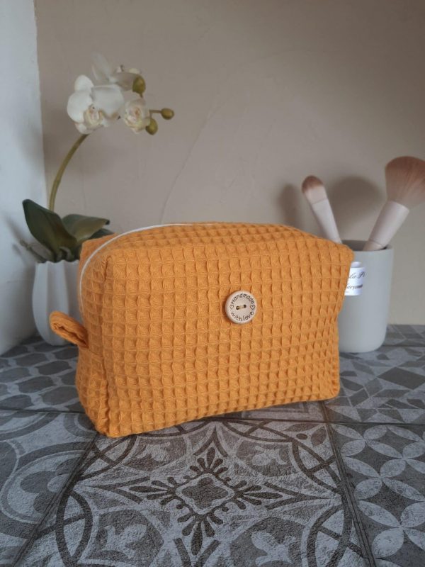 Trousse Essentiel en nid d'abeille moutarde, format compact avec zip doré et anse latérale. Un accessoire sobre et pratique pour ranger ses indispensables.