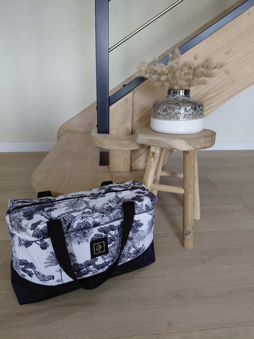 Sac week-end en toile imprimée sauvage, posé sur un tabouret en bois près d’un escalier moderne